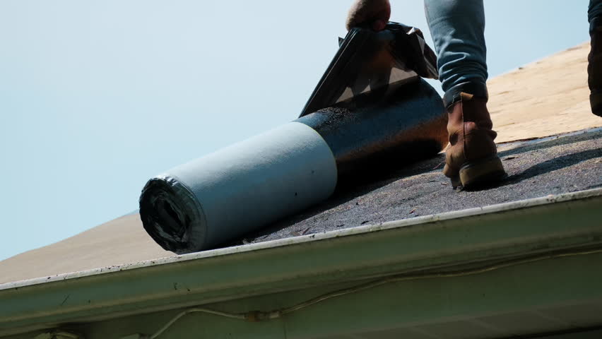 Roofer installing a new roof covering with glue surface on it. Self-Adhering Roofing System process.