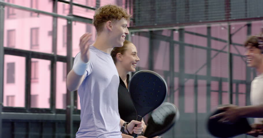 Group of diverse friends enjoying padel tennis on indoor court, smiling and holding rackets. Sports, recreation, friendship, teamwork, exercise, leisure