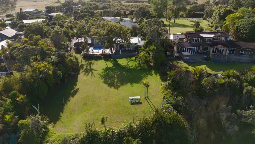 Luxury villas and mansion with large garden and Swimming pool at golden sunset in Muriwai beach, New Zealand. Aerial view.