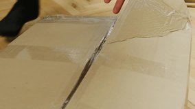 Man hands with sharp knife cut adhesive scotch tape on cardboard package in room closeup. Guy opens carton box to take out furniture parts at home. Unboxing process - Powered by Shutterstock - Get 15% off with code: PIKWIZARD15