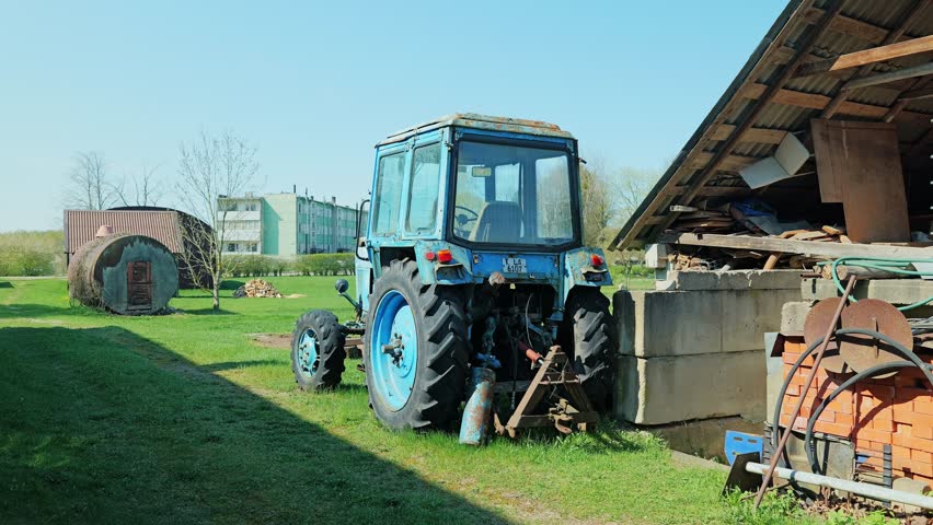 Iconic blue tractor parked near rustic barn reflects past era, rural field work