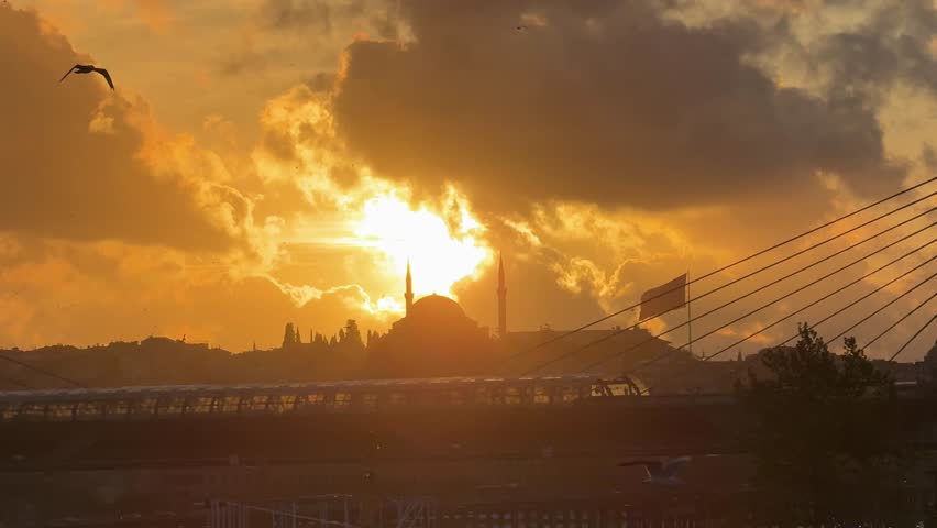 mosque silhouette at sunset with golden horn metro bridge in istanbul