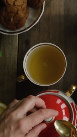 Vertical video. Drinking tea. Woman adding sugar to cup of brewed green tea. Top view