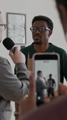 Vertical shot of woman filming interview in art gallery and holding smartphone with focus on screen