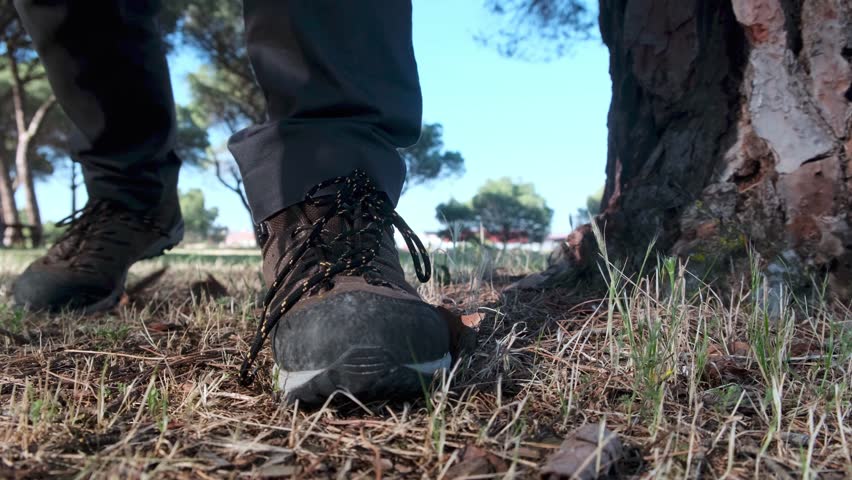 Close-up of a person tying trail boots while kneeling on dry grass, preparing for an outdoor hike or adventure.