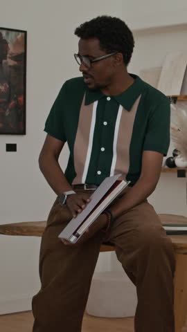 Vertical shot of Black man as artist showing artwork and prints to clients