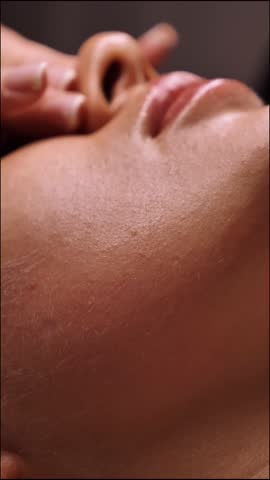 Beautician doing female anti-wrinkle rejuvenating facial massage in beauty salon, close-up, vertical