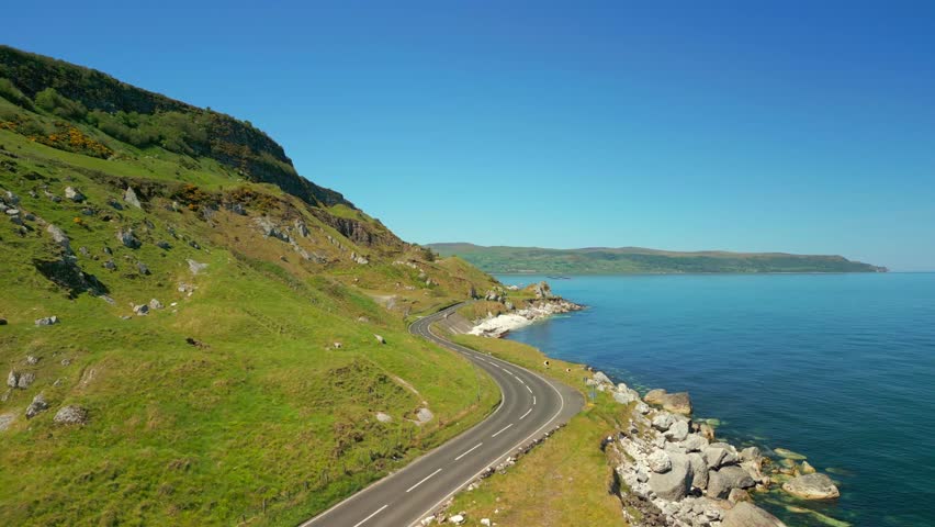 Aerial video of the Causeway Coastal Route at Glenarm in County Antrim, Northern Ireland, UK on a bright and sunny day. The camera travels over a road. Filmed in 4K, 60FPS and with Rec709 color.