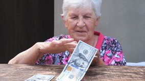 Portrait of happy grandmother holding bundle of money in hands and scattering foreign currency on the desk. Old smiling woman throwing one hundred dollar bills on the table. Close up Slow motion - Powered by Shutterstock - Get 15% off with code: PIKWIZARD15