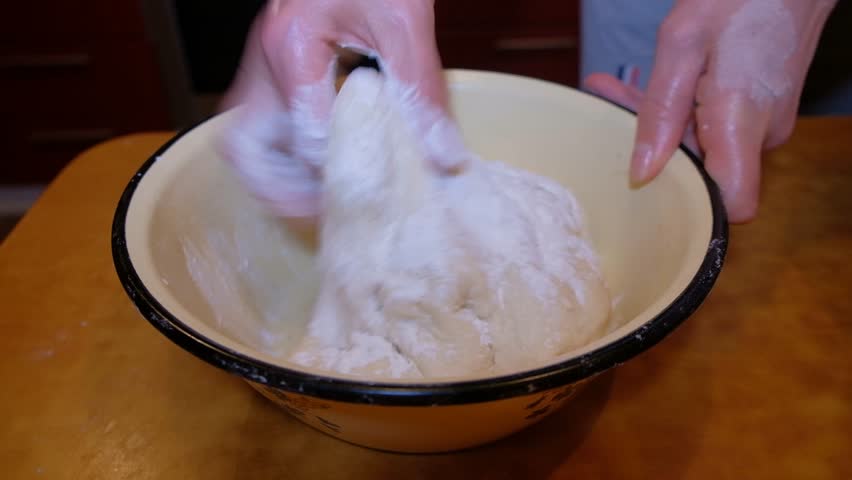 woman in apartment at home kneading dough to make pizza human hands visible product all actions on table dark color kneading dough with two hands and one