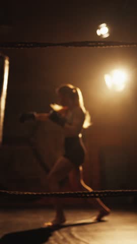 Cardio workout on boxing ring for stay slender, burn fat, female silhouette. Female fighter training hard in gym, practicing arms punches, striking punch bag, cinematic slow motion shot, do sport