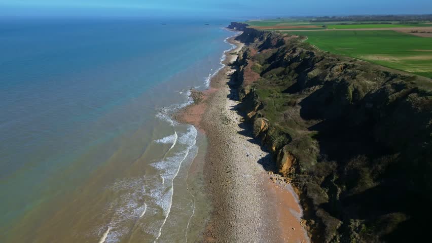 Coastal cliffs and sea at Longues-sur-Mer, Normandy, France. Aerial drone backward ascending