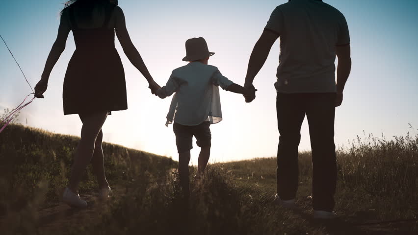 Carefree little boy holding hands of parents when walking in summer day in field . Man and woman lifting up his son, back view in countryside, happy family enjoy simple life, unforgettable moments