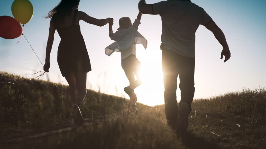 Carefree little boy holding hands of parents when walking in summer day in field . Man and woman lifting up his son, back view in countryside, happy family enjoy simple life, unforgettable moments