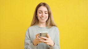Cheerful young woman using smartphone, engaging with digital content while standing against vibrant yellow background, embodying modern communication lifestyle - Powered by Shutterstock - Get 15% off with code: PIKWIZARD15