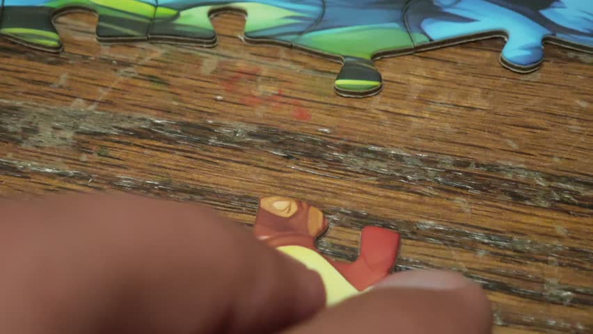 Close up of hands connecting colorful jigsaw puzzle pieces on a wooden table