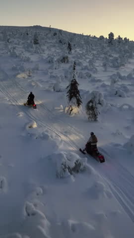 Portrait aerial tracking snowmobiles driving on a snowy mountain, polar night