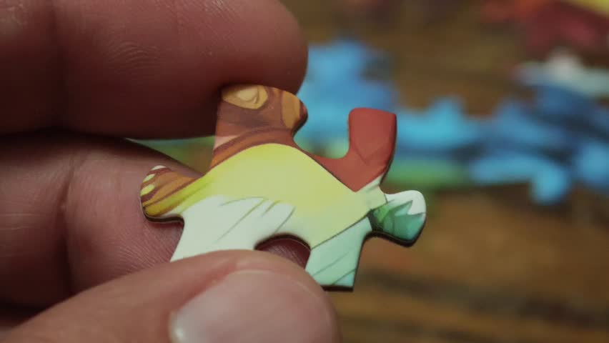 Close up of hands connecting two matching pieces of a colorful jigsaw puzzle on a wooden table