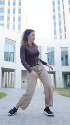 Contemporary dancer with curly hair performing dynamic modern choreography near sleek architectural structure, expressing creative energy through rhythmic movement