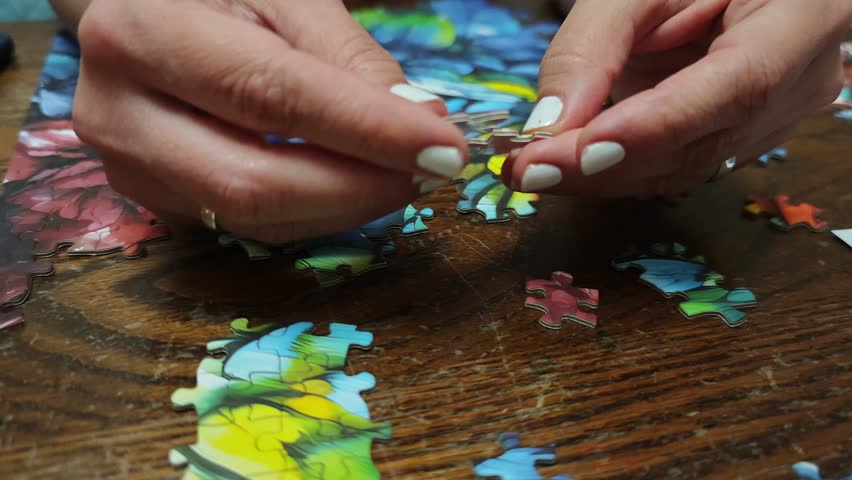 Woman joins colorful puzzle pieces on a wooden table, engaging in a relaxing pastime