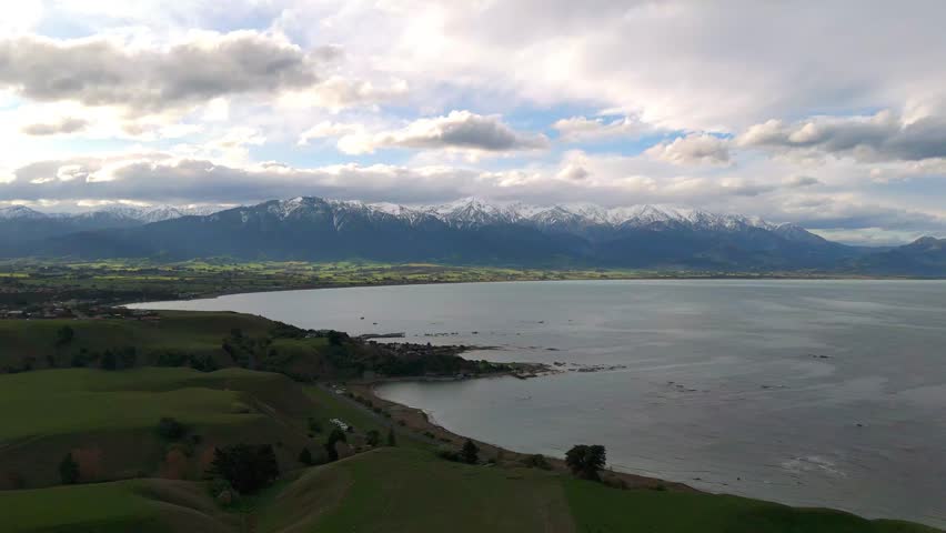 Forward drone flight reveals the coastal town of Kaikoura framed by the snow-covered peaks of the Southern Alps blending oceanfront scenery with dramatic alpine backdrops on New Zealand’s South Island