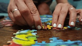 Female hands with white nail polish placing jigsaw puzzle pieces on a wooden table, assembling a colorful image - Powered by Shutterstock - Get 15% off with code: PIKWIZARD15