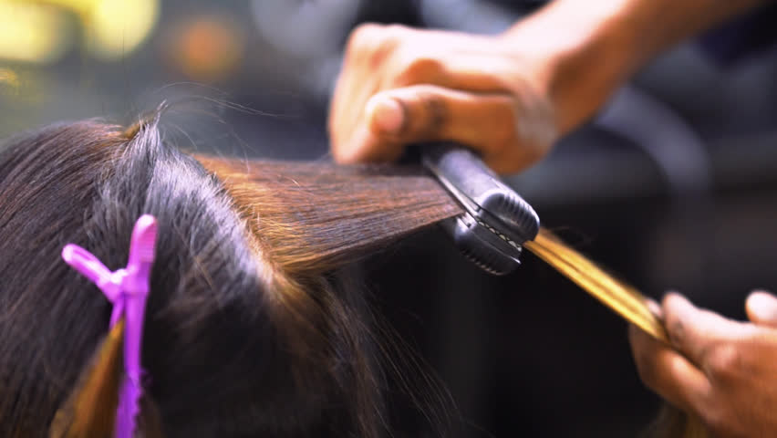 A stylist using a flat iron or straightener on hair.
