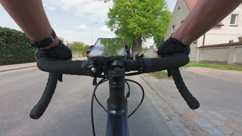 Cyclist riding bicycle through suburban street in summer with smartphone is mounted on handlebar for navigation during the ride. Healthy lifestyle and active outdoor sport