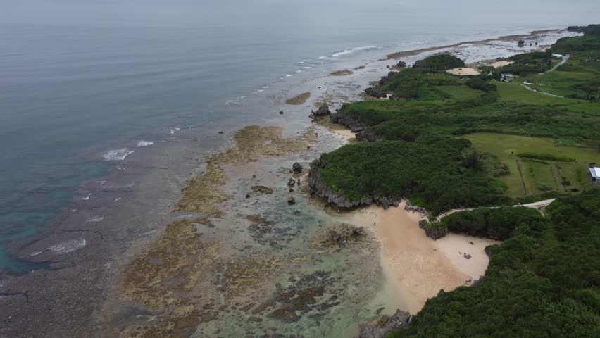 4K The serene seascape of Okinawa showcases crystal-clear waters, exposed rocky formations, and gentle waves lapping against the shore