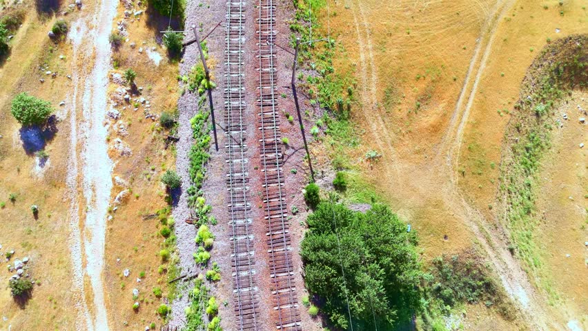Aerial view of railway tracks curving through a dry, hilly landscape with dirt roads nearby.