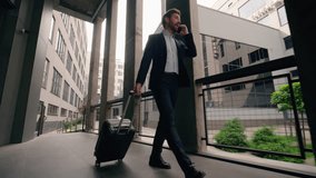 Adult professional male walking near office building airport going walk carrying baggage suitcase travel Caucasian man business trip guy businessman in city talking mobile phone communicate work job - Powered by Shutterstock - Get 15% off with code: PIKWIZARD15