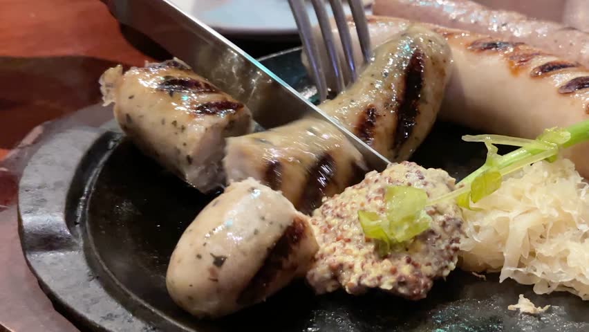 Close-up video of sausages being cut on a hot plate.