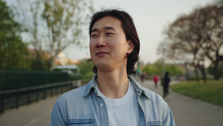Happy Asian man portrait outdoor in the city park. Young Korean guy cheerful male person looking smiling to camera 