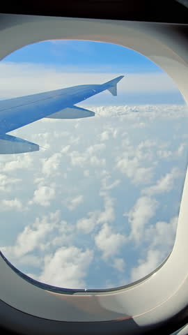 View Through Airplane Window of Wing and Clouds, Perspective from an airplane window showing the wing soaring over soft white clouds
