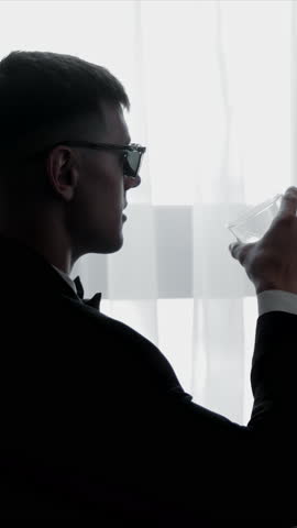 Man Drinking Wine in Silhouette by Window, Silhouetted man in formal attire drinks wine near a window,
