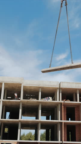 Construction Site with Crane Lifting Concrete Slab. A dynamic view of a construction site where a crane is lifting a concrete slab towards the upper levels of a building under construction.