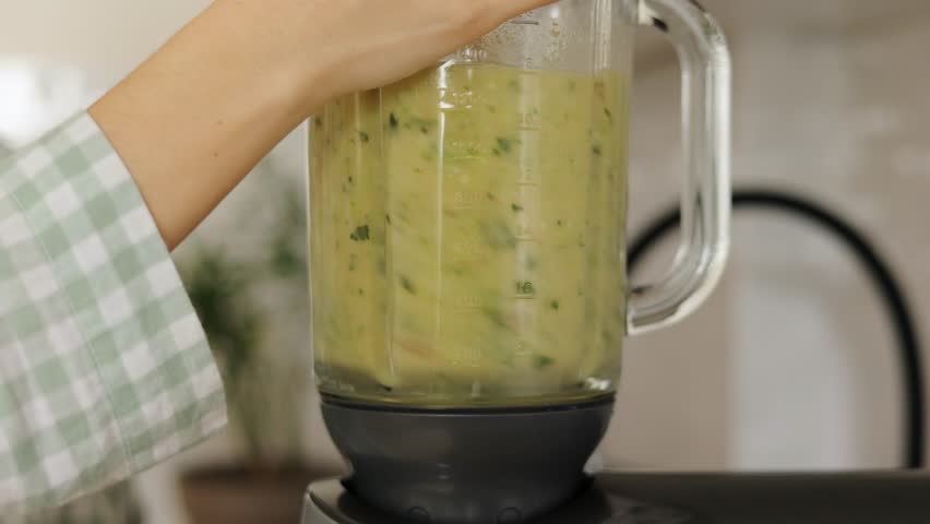woman turning on blender and making fresh fruit-greens smoothie in kitchen at home. Attractive housewife feel happy and relax, enjoy preparing healthy detox drink for breakfast in morning.