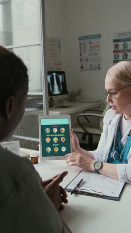 Vertical shot of female doctor with tablet and mature African American male patient discussing medical recommendations and rules of healthy living without diabetes