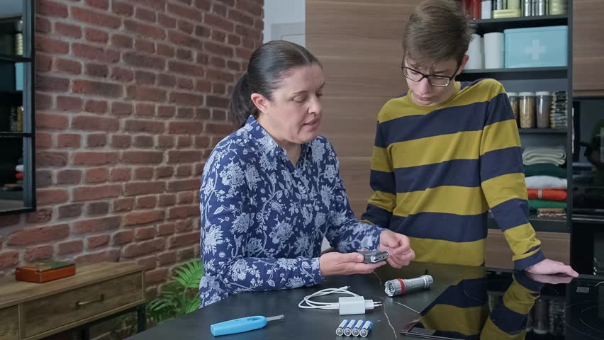 Mother teaching son how to use battery powered radio while checking emergency kit with lantern, lighter and charging cable. Family preparing 72 hours survival kit for disaster or electrical blackout.