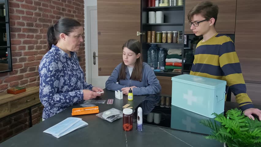 Mother teaching children how to use emergency medical supplies like injection, pills and disposable face masks. Family preparing 72 hour survival kit and checking medication stocked for disasters.