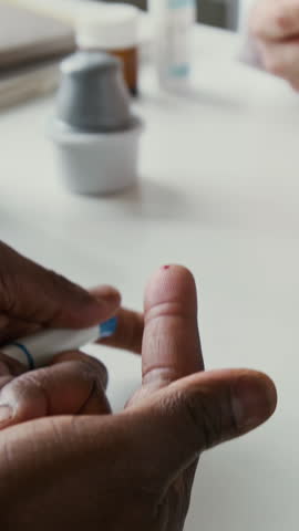 Vertical shot of hand of female doctor with glucose monitoring device checking blood sugar level of African American male patient with pricked finger