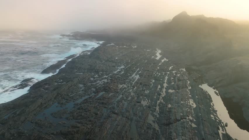Footage shows a rugged rocky coastline featuring igneous and metamorphic rock types, formed by geological processes of magma cooling and rock metamorphosis due to heat and pressure.