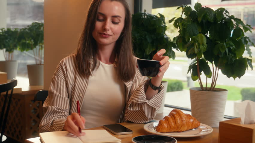 Young happy smiling inspiration business woman girl female businesswoman dreaming thinking working in cafe writing notes in notebook drinking coffee morning diary information write creative process