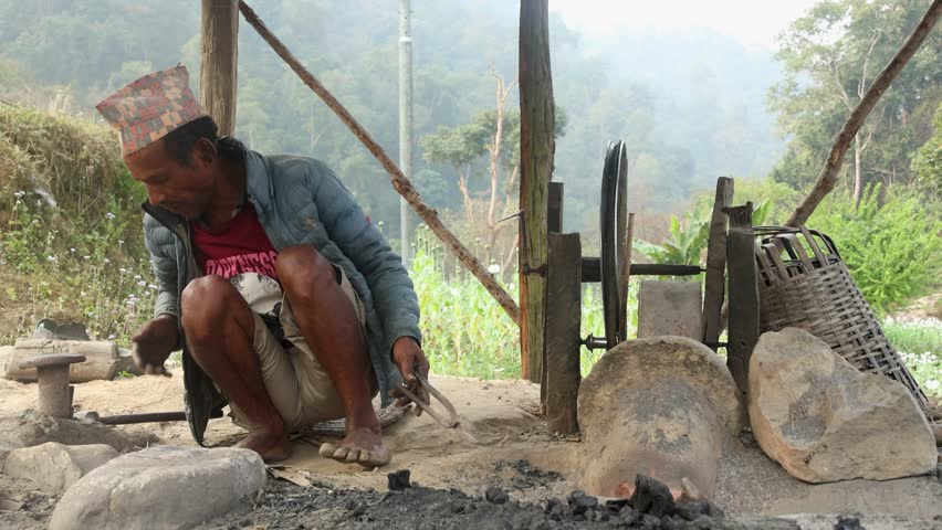 An old man is making a sickle in a traditional village blacksmith workplace. He heats the metal and shapes it with a hammer. Great for videos about rural life, tradition, or handmade tools.
