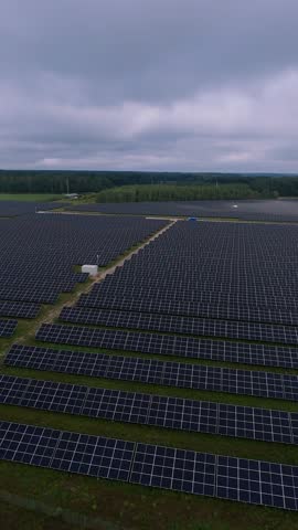 Vertical aerial view of large-scale solar farm with rows of dark blue solar panels arranged neatly across green fields representing renewable energy production, sustainability, and modern technology.