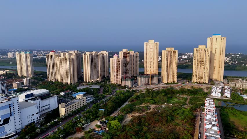 Aerial video showcases a modern, high-density residential complex with a clear sky above. Numerous tall, multi-story apartment towers, dominate the skyline. construction with visible cranes