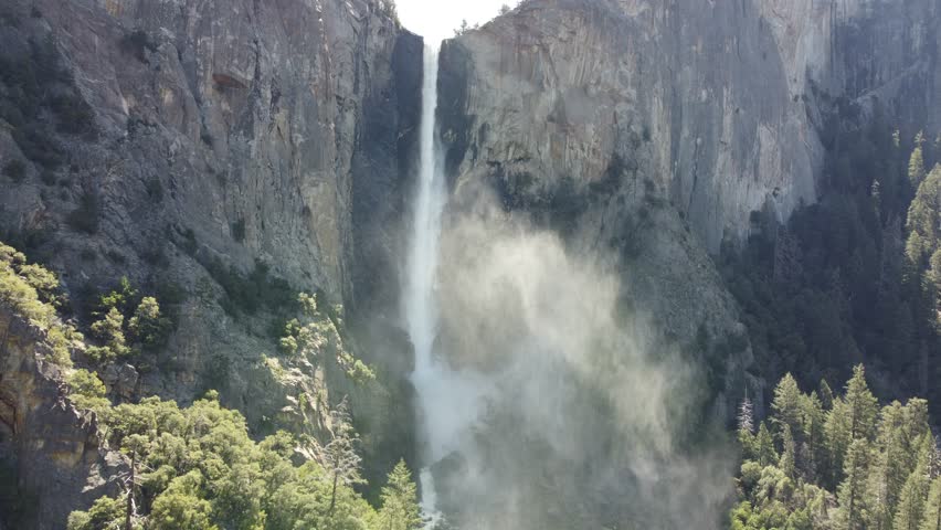 Sunlight Illuminating A Cascading Waterfall Spraying Mist Into The Mountain, Forest, And Valley Of Yosemite National Park, California, USA.