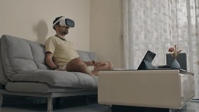 Man operating digital interface with VR headset while sitting on couch in living room - Powered by Shutterstock - Get 15% off with code: PIKWIZARD15