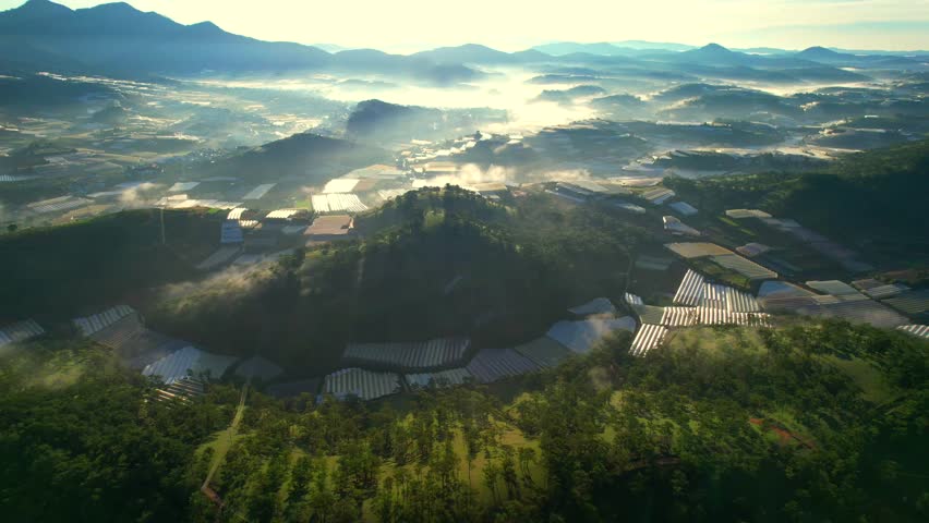 Sun rising over misty Dalat mountains, illuminating rolling hills, pine forests, and distant valleys shrouded in fog.