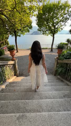 Woman in white dress walking toward Lake Como on a summer day